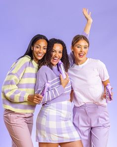 three young women posing for the camera with their arms in the air and one holding a cell phone