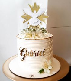 there is a white cake with gold lettering on it and flowers in the bottom tier