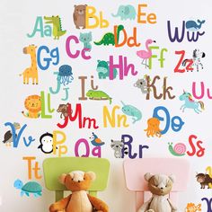 two teddy bears sitting in chairs next to a wall with letters and animals on it