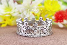 a close up of a silver crown ring on a table with flowers in the background