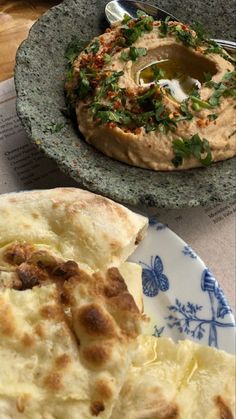 two plates with food on them sitting on a table next to a bowl of hummus