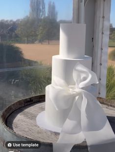 a three tiered white wedding cake with a large bow on top