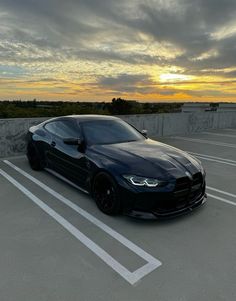 a black sports car parked in a parking lot with the sun going down behind it