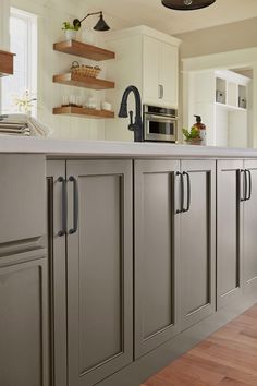 a kitchen with wooden floors and gray cabinets, white counter tops and open shelving