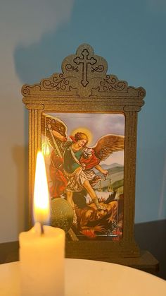 a lit candle sitting on top of a white table next to a framed angel painting