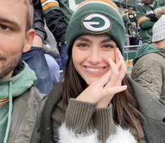 a woman wearing a green bay packers beanie and holding her hand to her face