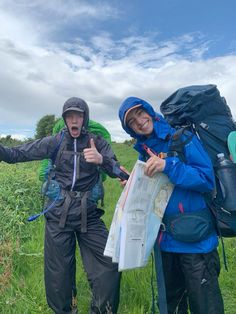 two people standing next to each other with backpacks on their shoulders and pointing at something