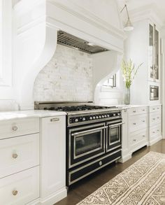 a white kitchen with an oven, range and rug on the floor in front of it