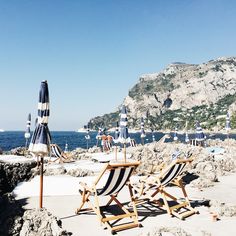 chairs and umbrellas on the beach with mountains in the background