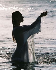 a woman standing in the water with her arms outstretched and holding something up to the sky