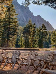 there are many wooden chairs lined up in the grass near some trees and mountain peaks