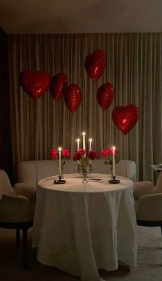 a table with candles and red heart balloons on it in front of a curtained window