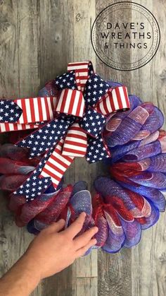 a patriotic wreath with red, white and blue mesh ribbons on it is being held up by someone's hand