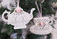 two ornaments hanging from a christmas tree decorated with lace and pink flowers, one teapot ornament