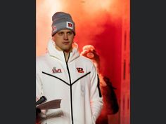 a man standing in front of a red background wearing a white jacket and grey hat