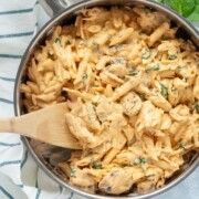 a pan filled with pasta and spinach on top of a white towel next to a wooden spoon