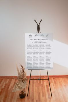 a wedding seating chart on a easel in front of a vase with dried flowers