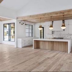 an empty kitchen with wooden floors and white cabinets in the center is surrounded by large windows