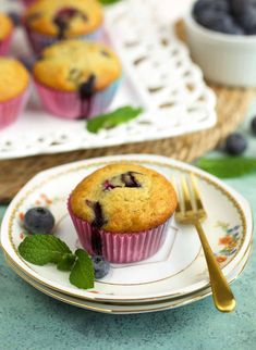 blueberry muffins on a plate with a fork and bowl of berries in the background