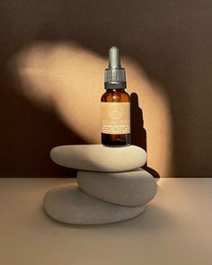 a bottle of essential oil sitting on top of two rocks with a shadow cast on the wall behind it