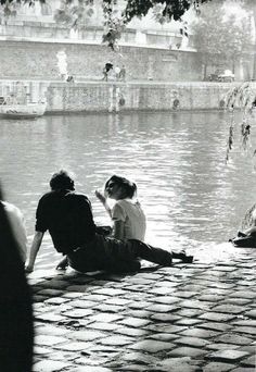 two people sitting on the ground next to a body of water