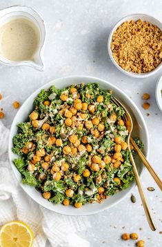 a white bowl filled with chickpeas and greens next to two bowls of dressing