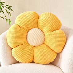 a yellow flower pillow sitting on top of a white chair next to a potted plant