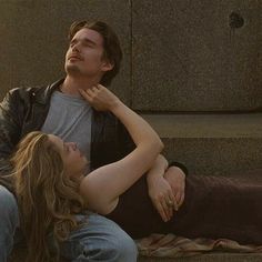 a man and woman laying on the ground next to each other with their arms around each other