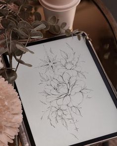 a drawing is sitting on a table next to some flowers and a cup with a straw in it