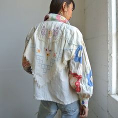 a woman standing in front of a window wearing a white jacket with colorful designs on it