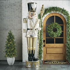 a large nutcracker standing in front of a door with a wreath on it