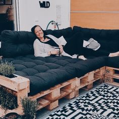 a woman sitting on top of a couch made out of wooden pallet boards and black cushions