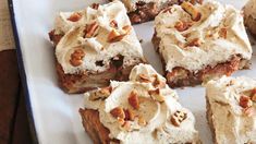 several pieces of dessert sitting on top of a white platter with frosting and nuts