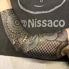 a man with a tattoo on his arm and hand is sitting in front of a sign that reads nissaco