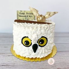 an owl cake is decorated with white frosting and yellow eyes, which are adorned with gold leaf accents