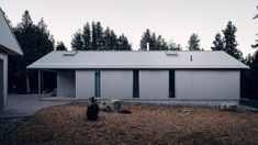 a house with two garages and trees in the back ground, surrounded by gravel