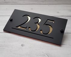 a black house number sign with gold numbers on the front and back of it, sitting on a white wood floor