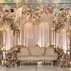 a couch sitting under a white and pink flower covered arch with chandelier behind it