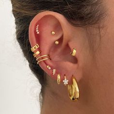 a close up of a person wearing gold ear cuffs and piercings on their ears