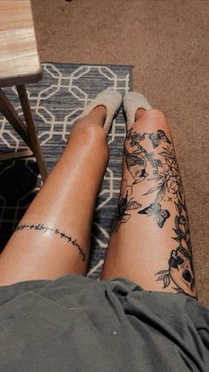 a woman's legs with tattoos on them sitting in front of a table and chair