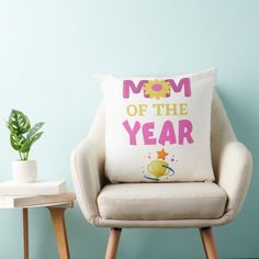 a chair with a pillow that says mom of the year next to a potted plant