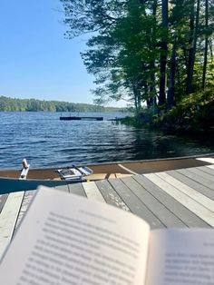 an open book sitting on top of a wooden dock next to a body of water