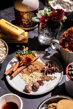 an assortment of spices on a plate next to cups and bowls with flowers in them