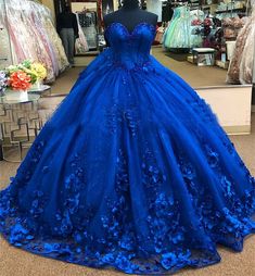 Embrace the magic of your quinceanera with this exquisite royal blue ball gown. The dramatic ball gown is crafted from luxurious tulle, and offers a voluminous, fairy-tale look, while the chapel train adds a regal flair, perfect for your grand entrance. The strapless neckline creates an elegant and timeless look, highlighting your shoulders and neckline with sophistication. What truly sets this gown apart are the stunning 3D flowers and applique detailing, which delicately adorn the bodice and s Floral Quince Dress, Royal Blue Princess Dress, Royal Blue Quince Dress, Floral Quince, Royal Blue Ball Gown, Ball Gown Sweet 16, Royal Blue Quinceanera Dresses, Royal Blue Quince, Royal Blue Quinceanera