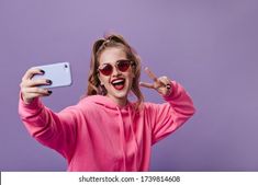 a woman in sunglasses taking a selfie with her cell phone while wearing a pink hoodie