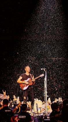 a man standing on top of a stage with a guitar in front of an audience