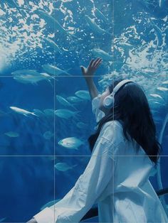 a woman wearing headphones standing in front of a large aquarium tank with fish swimming around