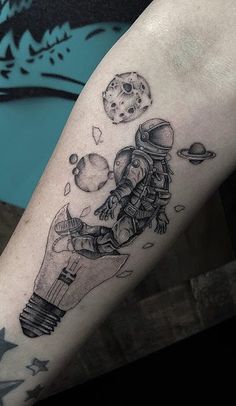 a tattoo on the arm of a person with an astronaut's hand holding a light bulb