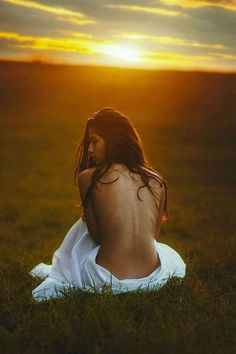 a woman sitting in the grass at sunset