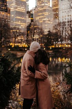 two people standing next to each other in front of a lake and tall buildings at night